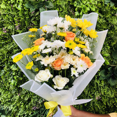 Bouquet of yellow, white, and orange flowers with a clear wrap on a green grass background